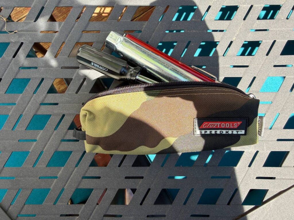 A camouflage CruzTools SpeedKit tool roll unzipped with chrome wrenches and a tire iron laid beside it