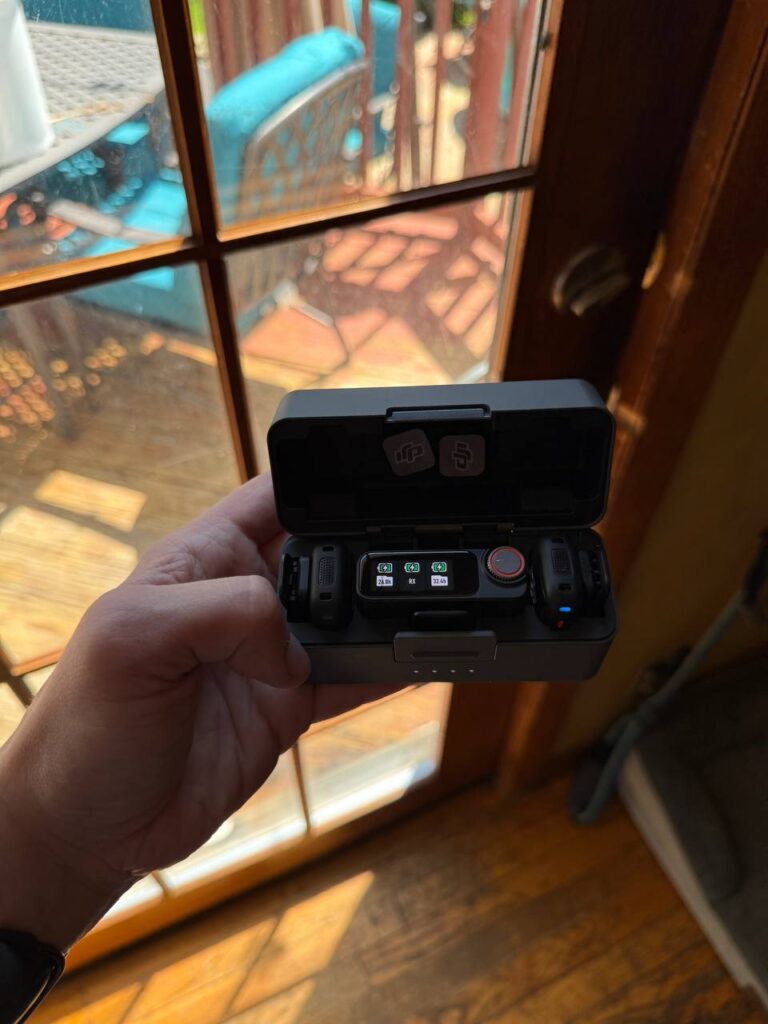 A DJI Mic 3 wireless microphone kit held open in its charging case, showing both transmitters and the receiver