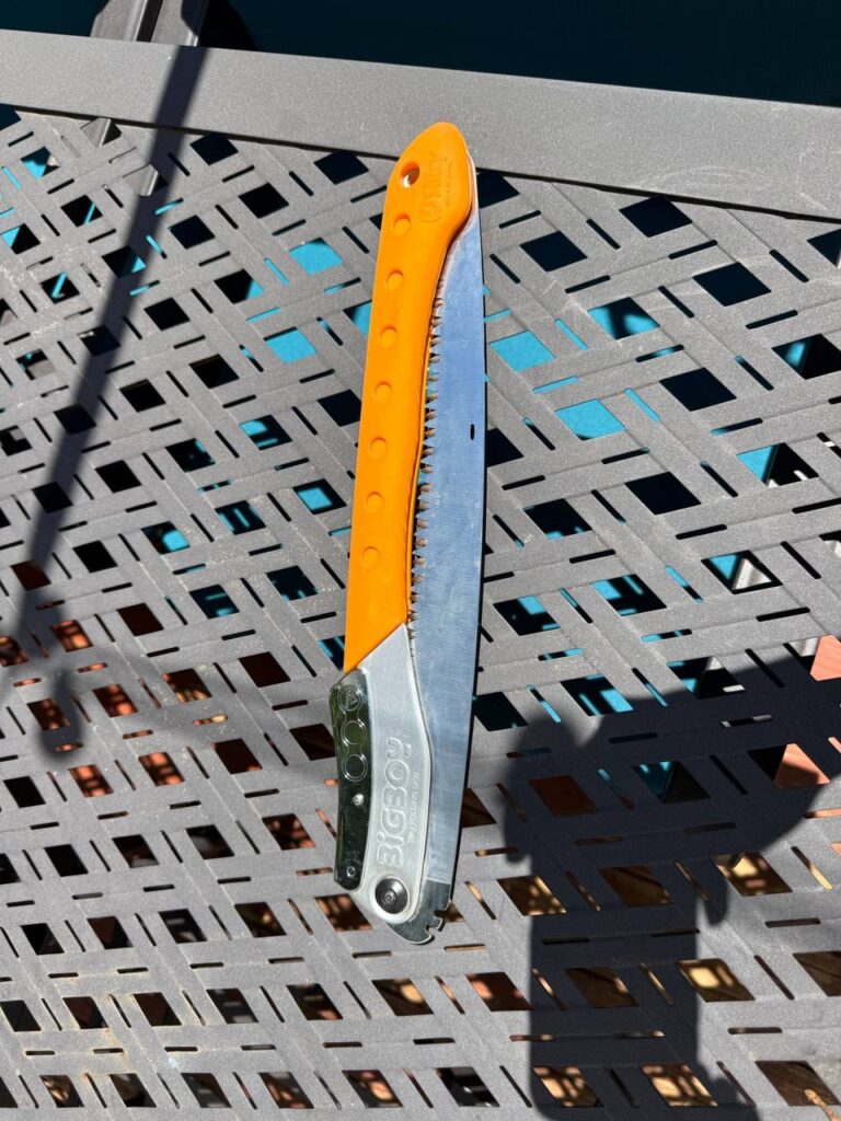 A Silky BigBoy folding saw with an orange handle, blade open, resting on a metal table