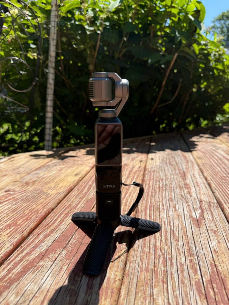 An XTRA Muse pocket gimbal camera standing on a small tripod on a wooden deck