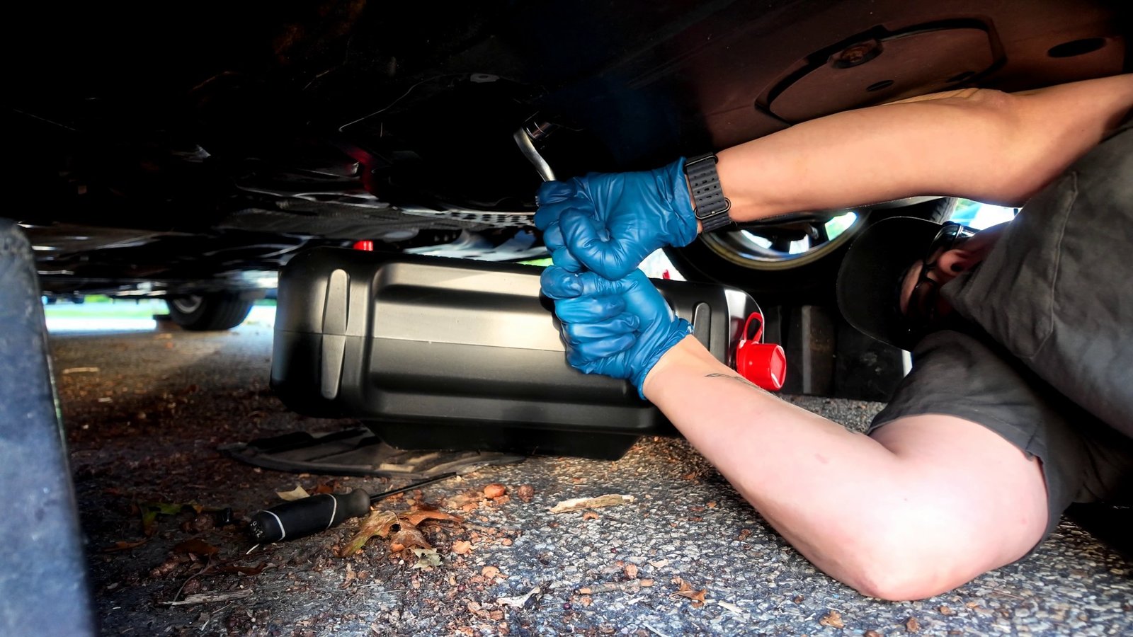 Gloved hands breaking the Mazda 3 drain plug loose with a ratchet over the drain pan