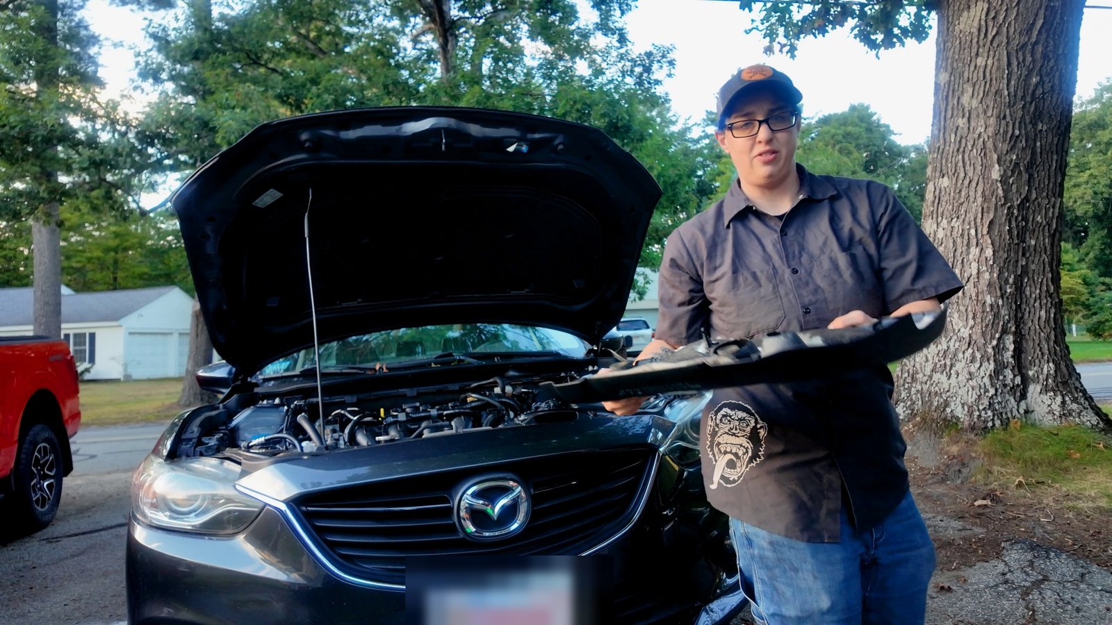 Emily holding the Mazda 6 engine cover she just removed, hood up