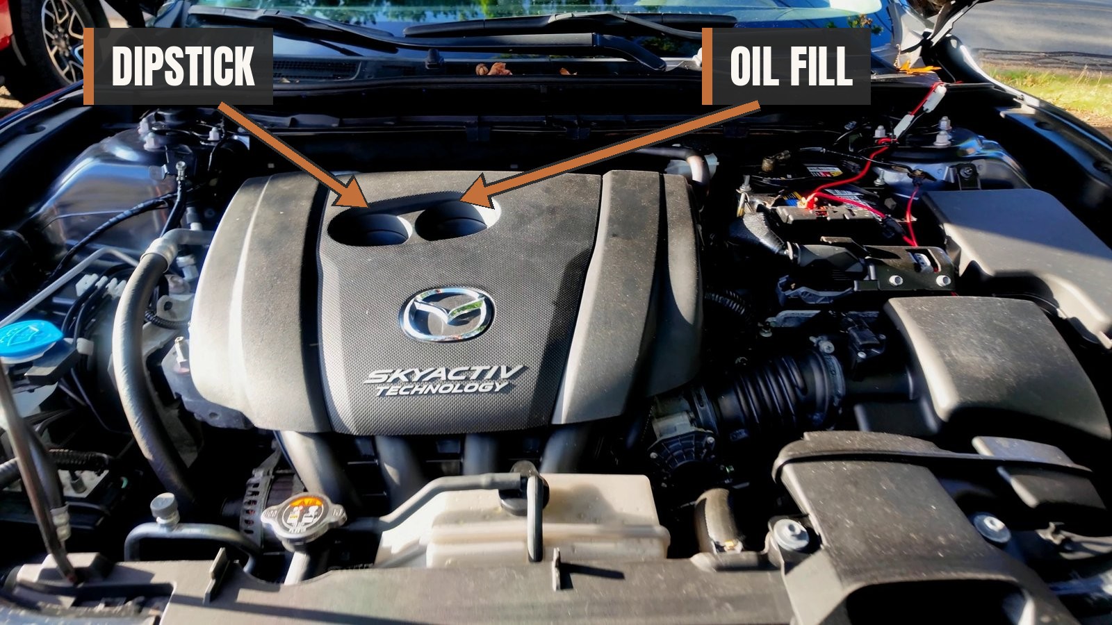 Mazda 3 SKYACTIV 2.0L engine bay with arrows marking the dipstick (left hole) and the oil fill (right hole)
