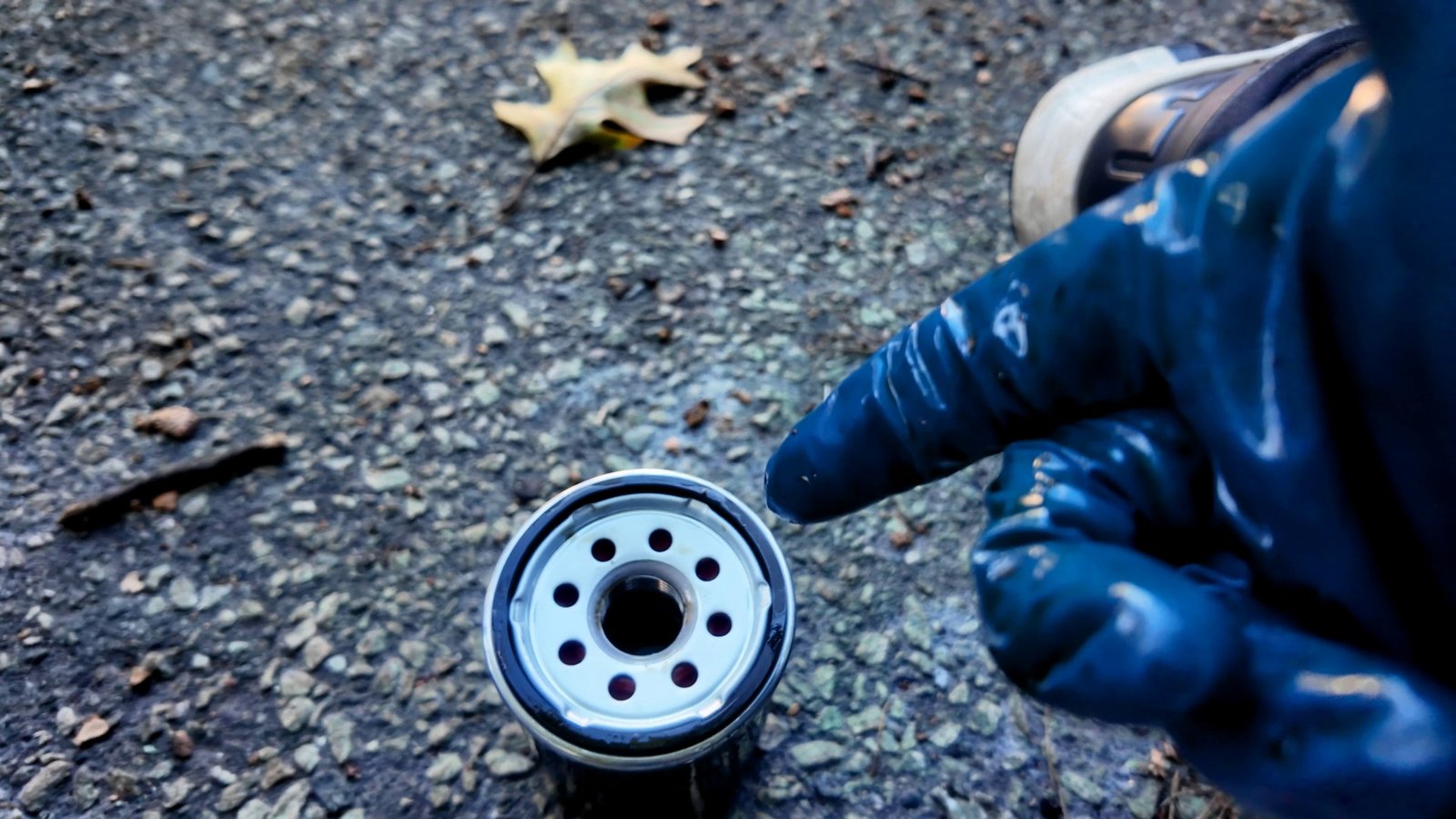 Gloved finger pointing at the rubber seal on an oil filter
